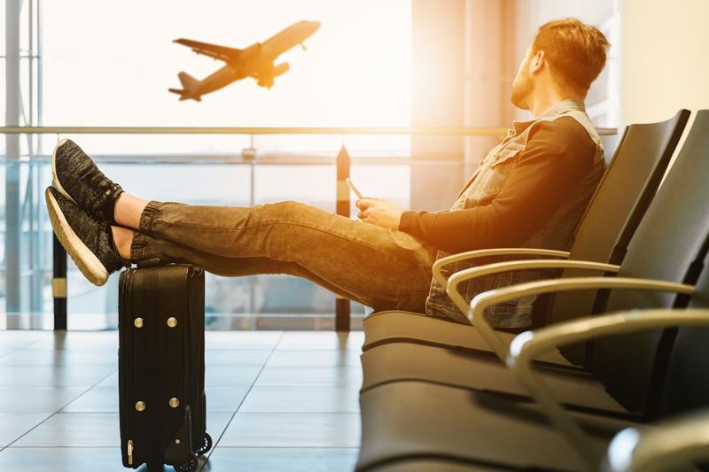 man waiting at airport feet up watching plane taking off